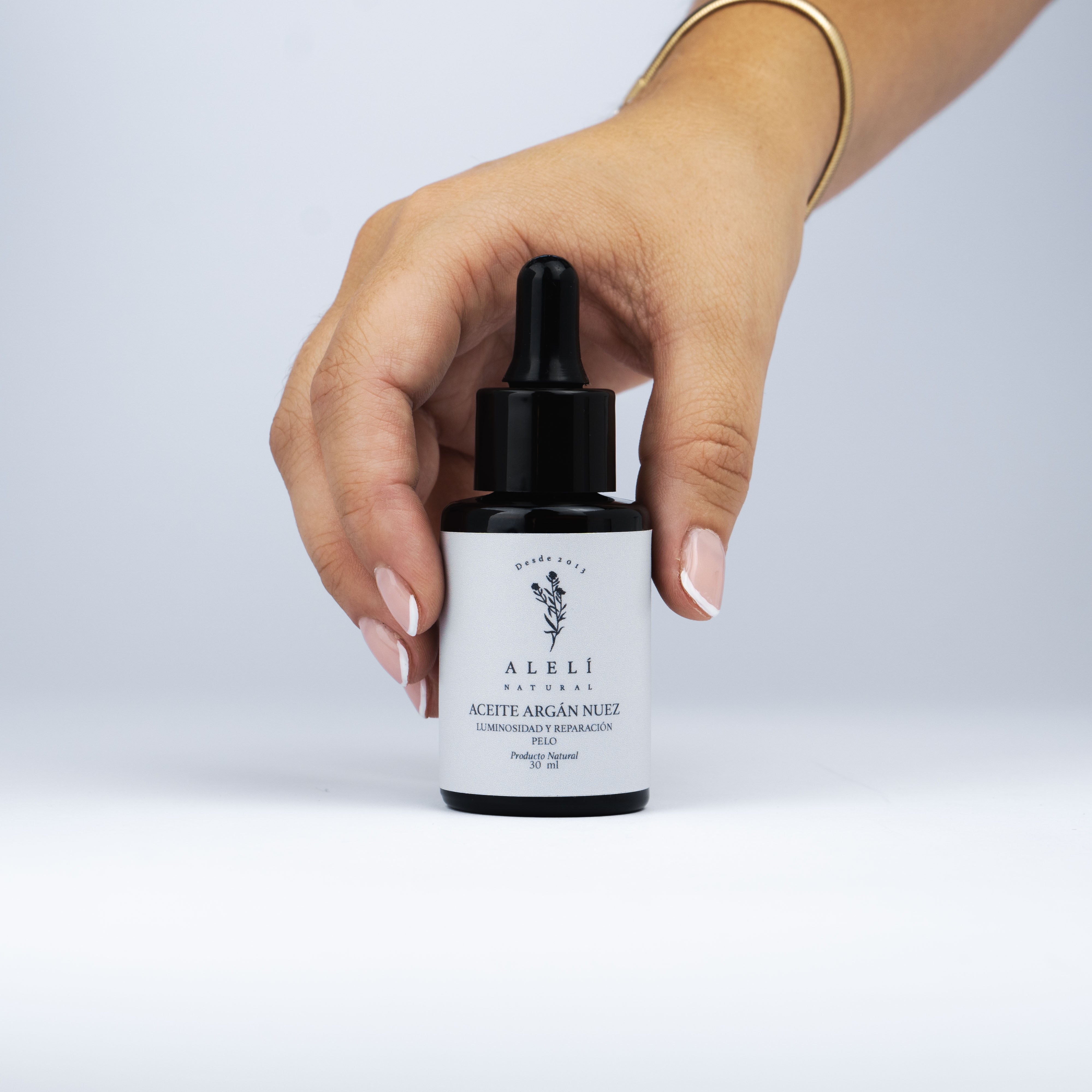 Aceite Capilar de Argán Nuez Alelí Natural sostenido en una mano, mostrando tamaño y presentación.