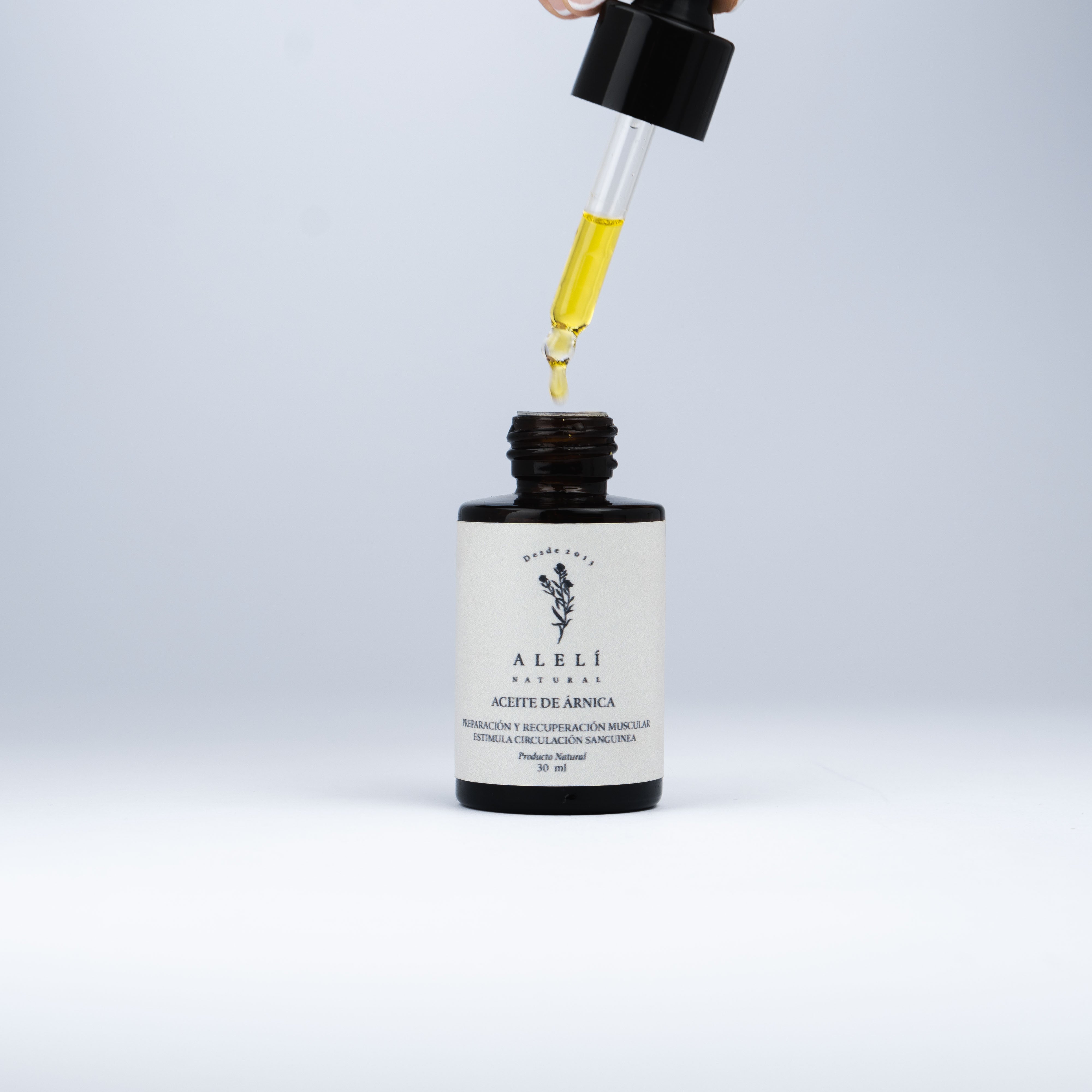 Aceite de Árnica Alelí Natural con gotero aplicando el producto desde el frasco abierto.